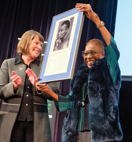 Provost Lisa Lynch applauds as Hortense Spillers lifts up a large framed plaque. 
